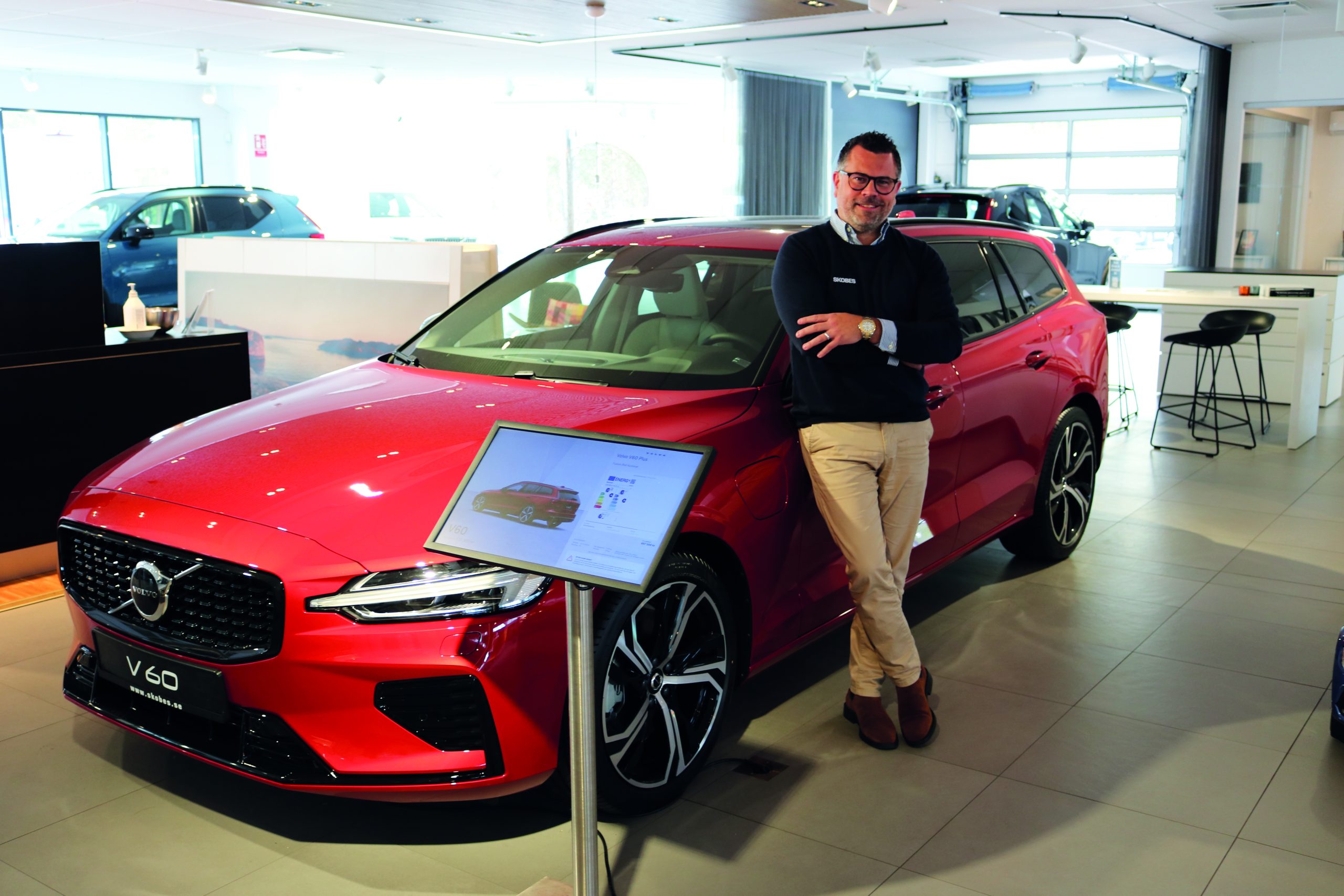 Bilden visar Christoffer Dahlberg, försäljningschef på Skobes Bil AB i Västervik. Han står bredvid en röd Volvo V60 i bilhallen.